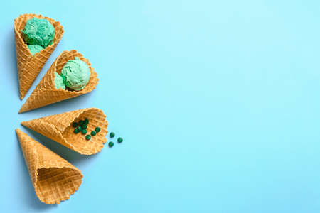 Tasty spirulina ice-cream and waffle cones on color background
