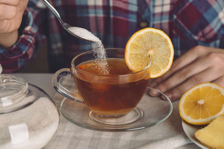 Woman pouring sugar into cup with hot tea at table, closeupの写真素材