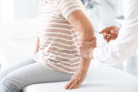 Doctor giving mature woman with joint pain injection in clinicの写真素材