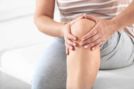 Mature woman suffering from pain in knee in clinic, closeup