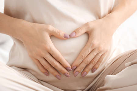 Beautiful young pregnant woman making heart with her hands, closeupの写真素材