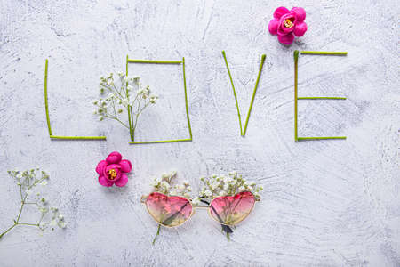 Composition with word LOVE, flowers and sunglasses on light background