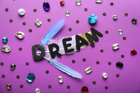 Word DREAM with precious stones on color background