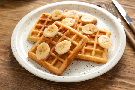 Plate with tasty waffles and banana on tableの写真素材