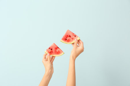 Female hands with pieces of juicy watermelon on color backgroundの写真素材