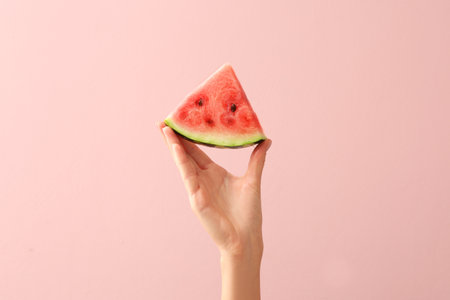 Female hand with piece of juicy watermelon on color backgroundの写真素材