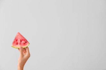 Female hand with piece of juicy watermelon on light backgroundの写真素材