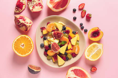 Plate with tasty fruit salad on color background