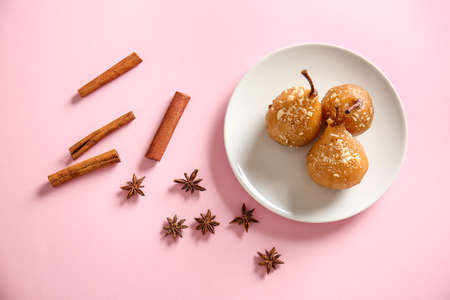 Plate with tasty cooked pears and spices on color background