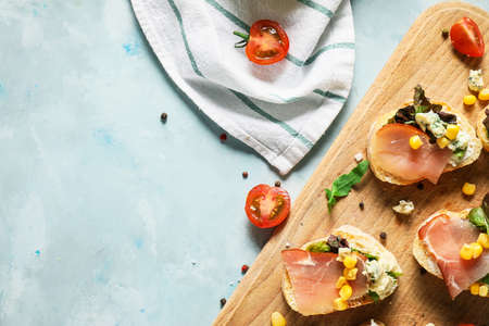 Wooden board with tasty sandwiches on color background