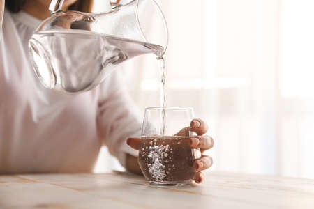 Woman pouring fresh water from jug into glass on table