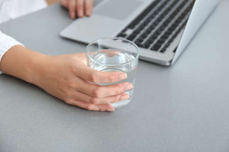 Woman with glass of fresh water and laptop working in office, closeupの写真素材