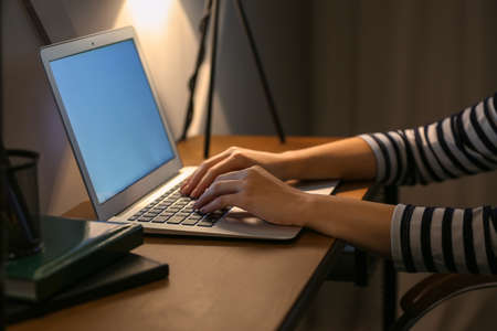 Young woman working on laptop at table in eveningの写真素材