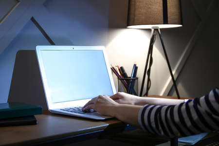 Young woman working on laptop at table in evening