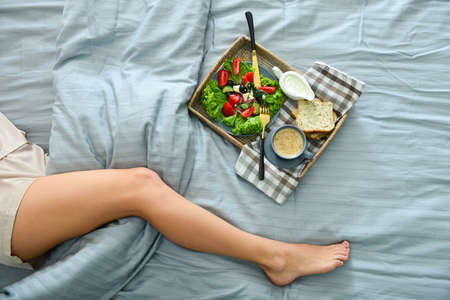 Tray with tasty breakfast on bed of young womanの写真素材