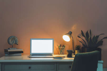 Modern stylish workplace with laptop near color wall at nightの写真素材