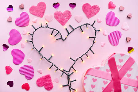 Heart made of glowing garland and gift on color backgroundの写真素材