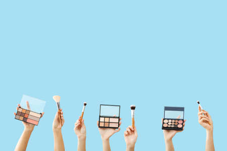 Many hands with decorative cosmetics and makeup brushes on color backgroundの写真素材