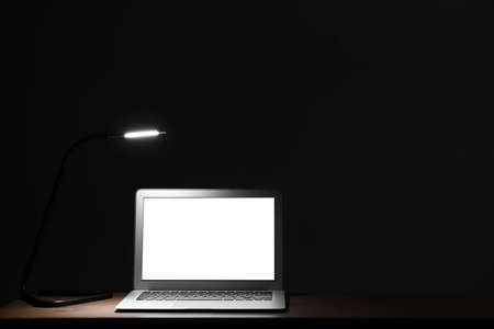 Glowing laptop with lamp on table at nightの写真素材