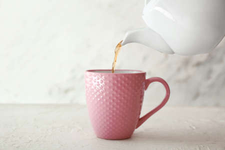 Pouring of hot tea from teapot into cup on tableの写真素材