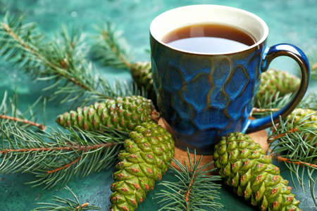 Cup of hot tea with cones and fir tree branches on color backgroundの写真素材