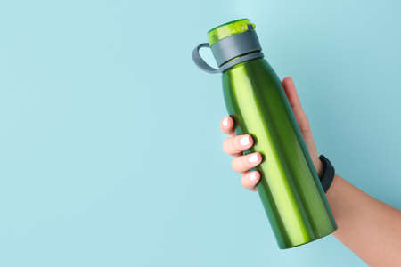 Female hand with sports water bottle on color background