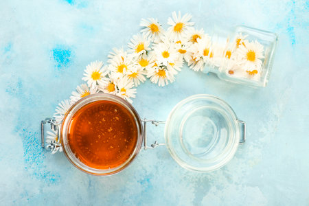 Jars with honey and chamomile flowers color backgroundの写真素材
