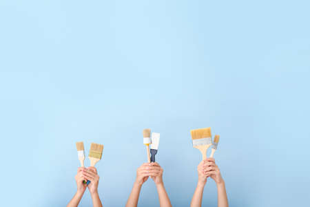 Female hands with paint brushes on color background