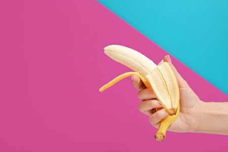 Female hand with ripe peeled banana on color backgroundの写真素材