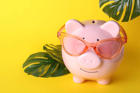 Piggy bank with sunglasses and tropical leaves on color backgroundの写真素材