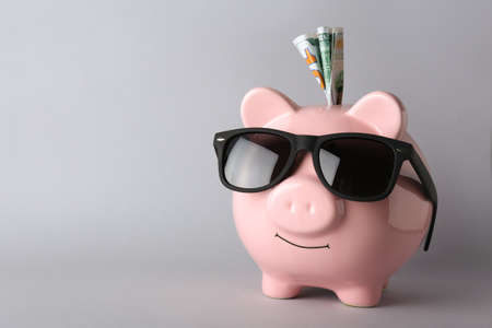 Piggy bank with sunglasses and money on gray backgroundの写真素材
