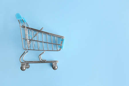 Empty small shopping cart on color background