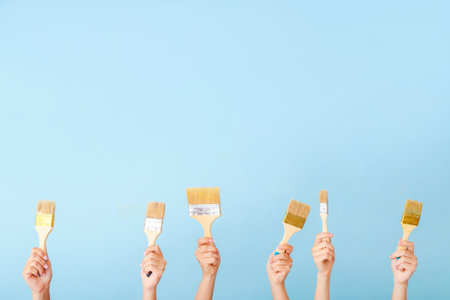 Female hands with paint brushes on color backgroundの写真素材