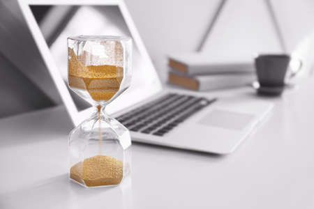 Hourglass and laptop on table in roomの写真素材