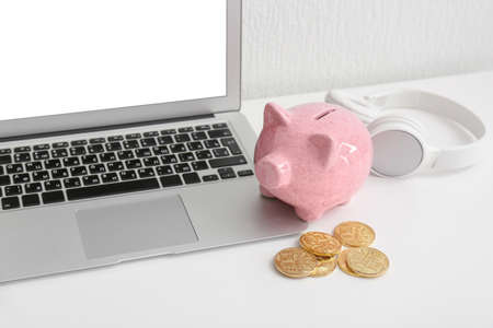 Piggy bank with laptop an coins on tableの写真素材