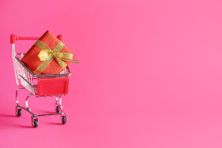 Small shopping cart with gift box on color backgroundの写真素材