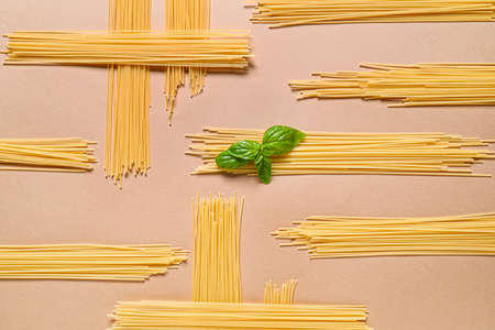 Dry pasta with basil on color background