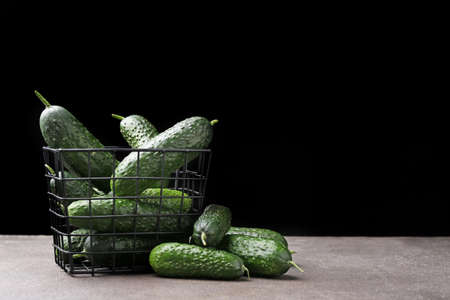 Basket with fresh green cucumbers on table against dark backgroundの写真素材