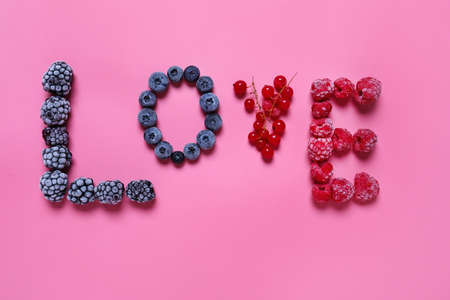 Word LOVE made of frozen berries on color background