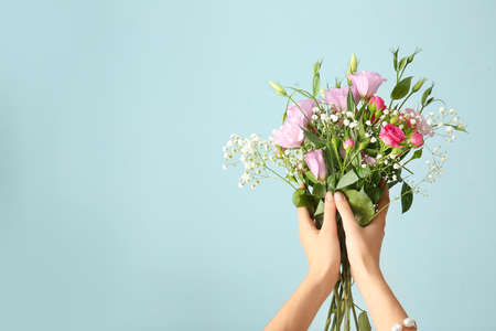 Female hands with bouquet of beautiful flowers on color backgroundの写真素材