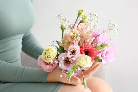 Woman with bouquet of beautiful flowers on light backgroundの写真素材