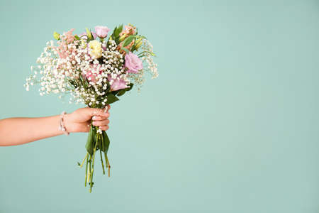 Female hand with bouquet of beautiful flowers on color backgroundの写真素材