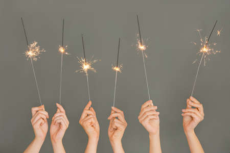Female hands with Christmas sparklers on gray backgroundの写真素材