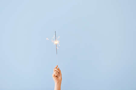 Female hand with Christmas sparkler on color backgroundの写真素材