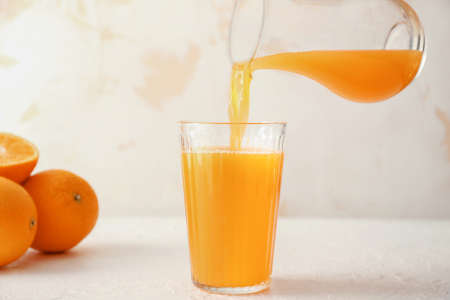 Pouring of fresh orange juice from jug into glass on tableの写真素材