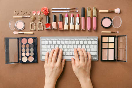 Hands of female beauty blogger with PC keyboard and set of decorative cosmetics on color backgroundの写真素材