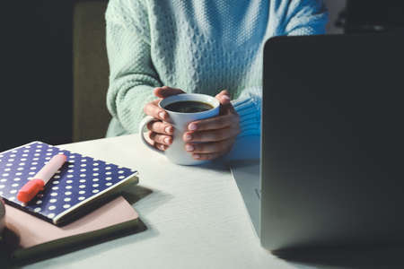 Young woman drinking coffee while working in office late in eveningの写真素材
