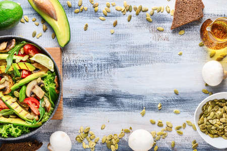 Frying pan with tasty avocado salad and ingredients on wooden background