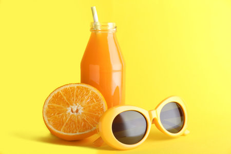 Bottle of fresh orange juice with sunglasses on color backgroundの写真素材
