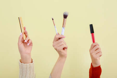 Many hands with decorative cosmetics and brushes on color background